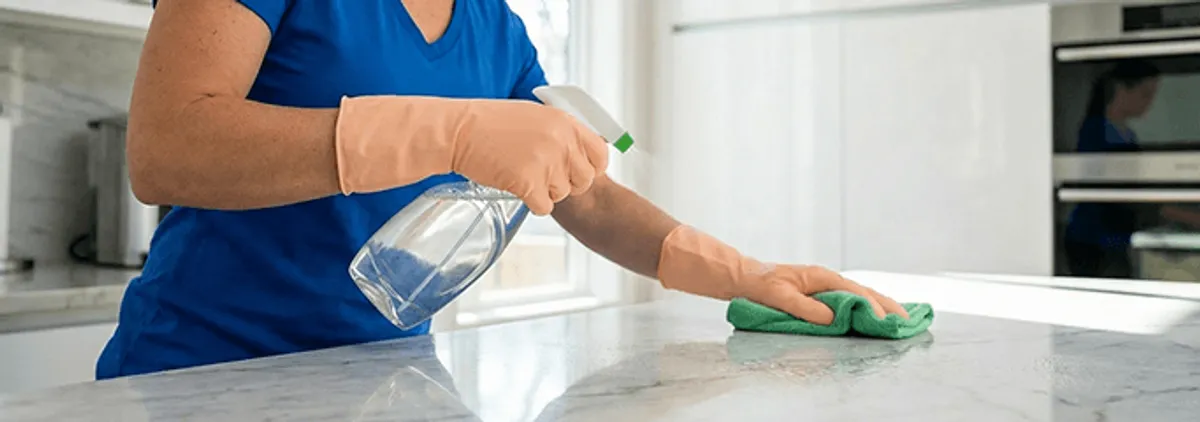 Maid service worker spraying and wiping a kitchen countertop with a microfiber cloth for sanitizing, Providence, RI.